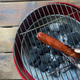 Overhead view of tongs holding well-done hot dog over camping grill